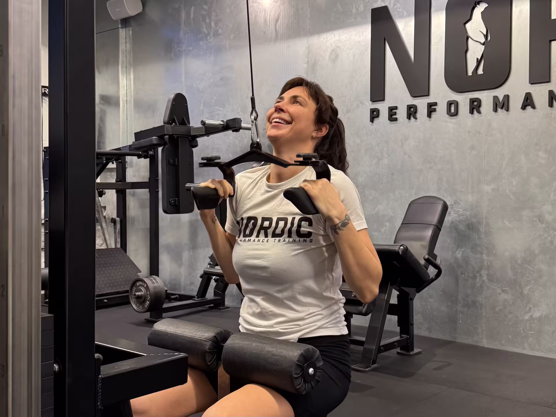 Woman in her 30s smiling during cable pulldowns with her personal trainer in Copenhagen.