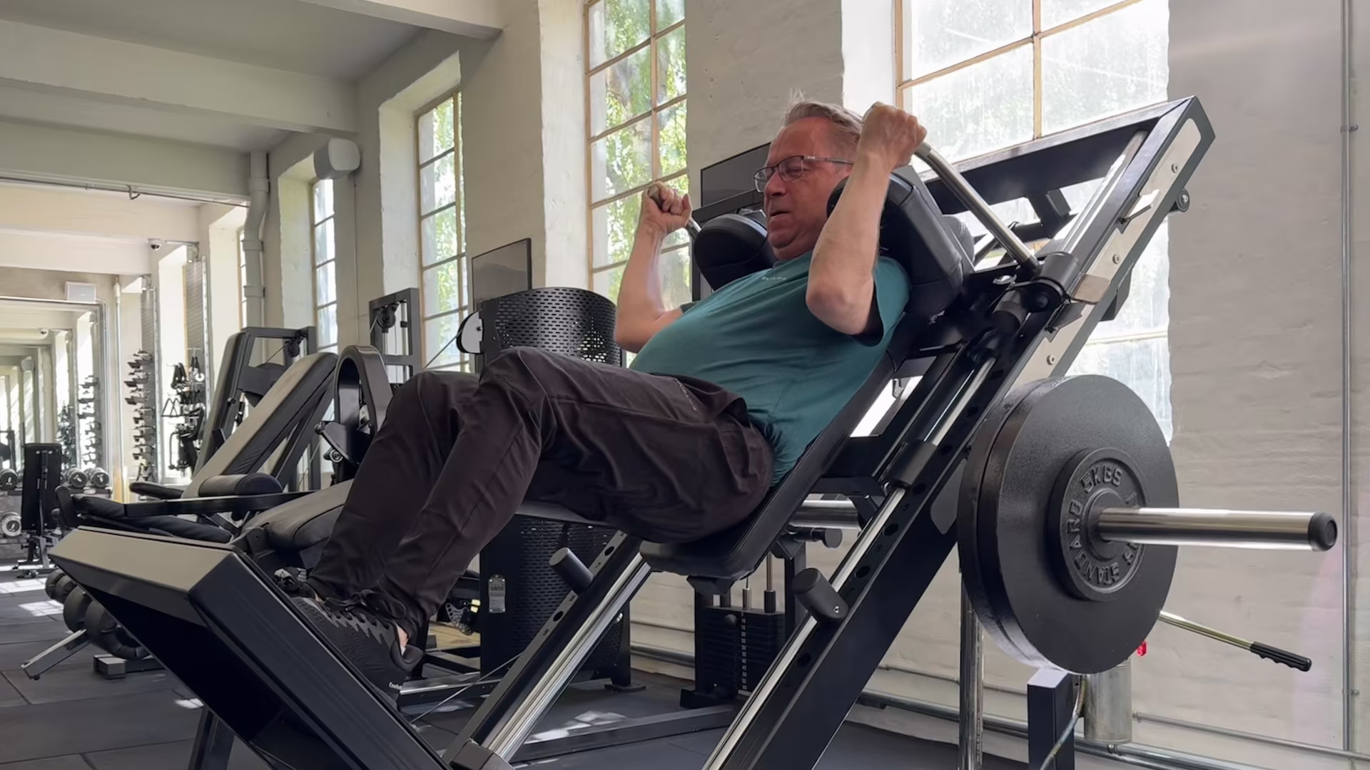 Klient med slidgigt udfører sikkert hack squats hos Nordic Performance Training med sin personlige træner og fysioterapeut.