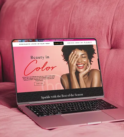 Laptop displaying a vibrant beauty website on a pink couch, featuring a smiling woman and the headline “Beauty in Color,” promoting seasonal cosmetic products.