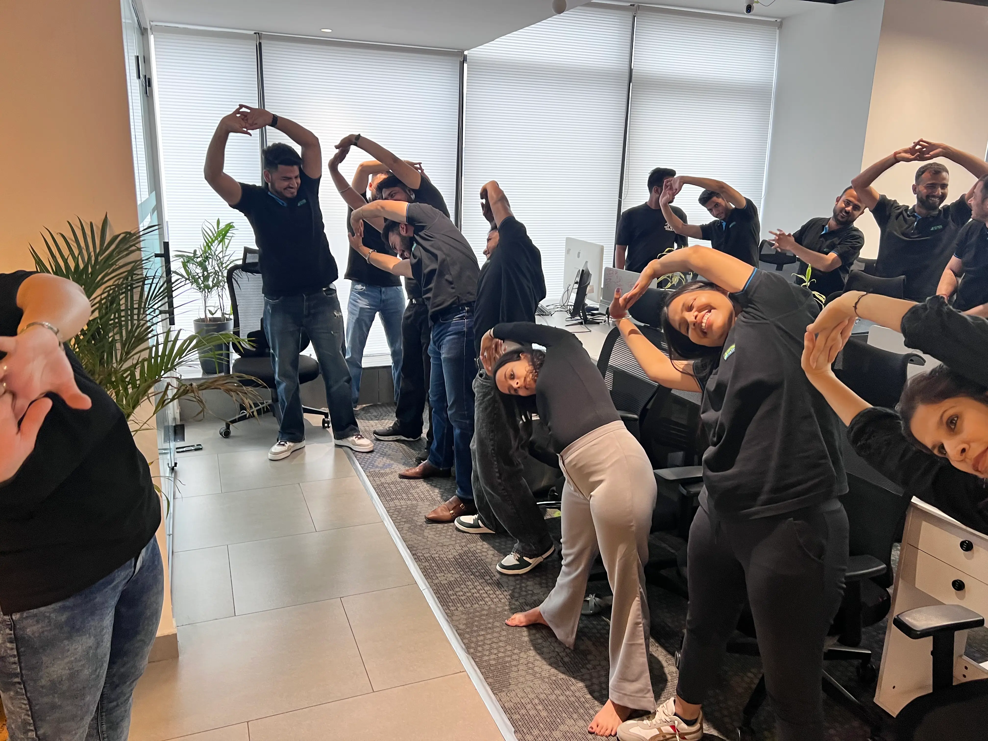 Office team practicing side stretch yoga poses together at their desks, promoting workplace wellness, relaxation, and team bonding through mindful movement.