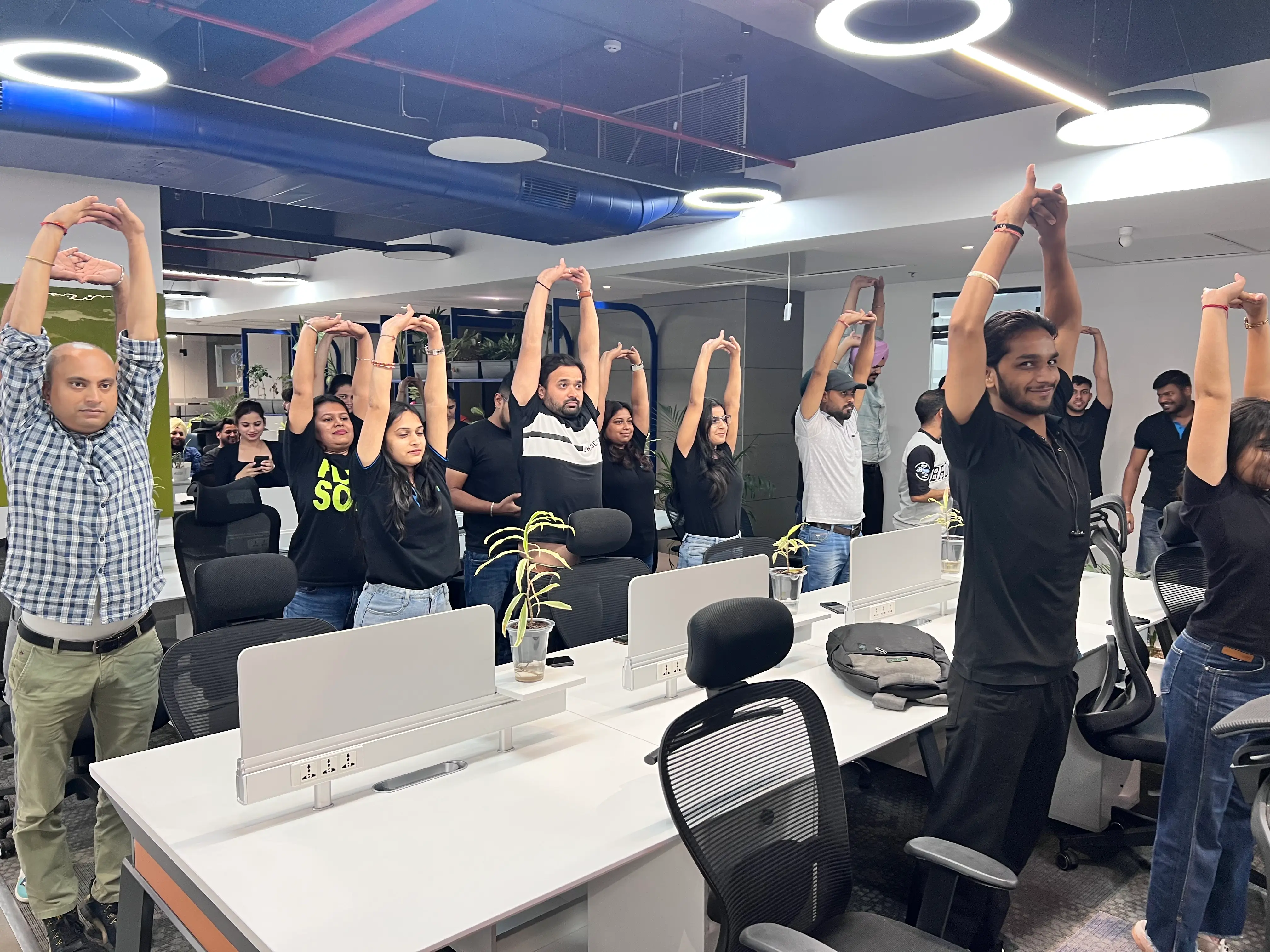 Team members practicing a group yoga stretch session in a modern office environment, promoting wellness, mindfulness, and healthy workplace culture.