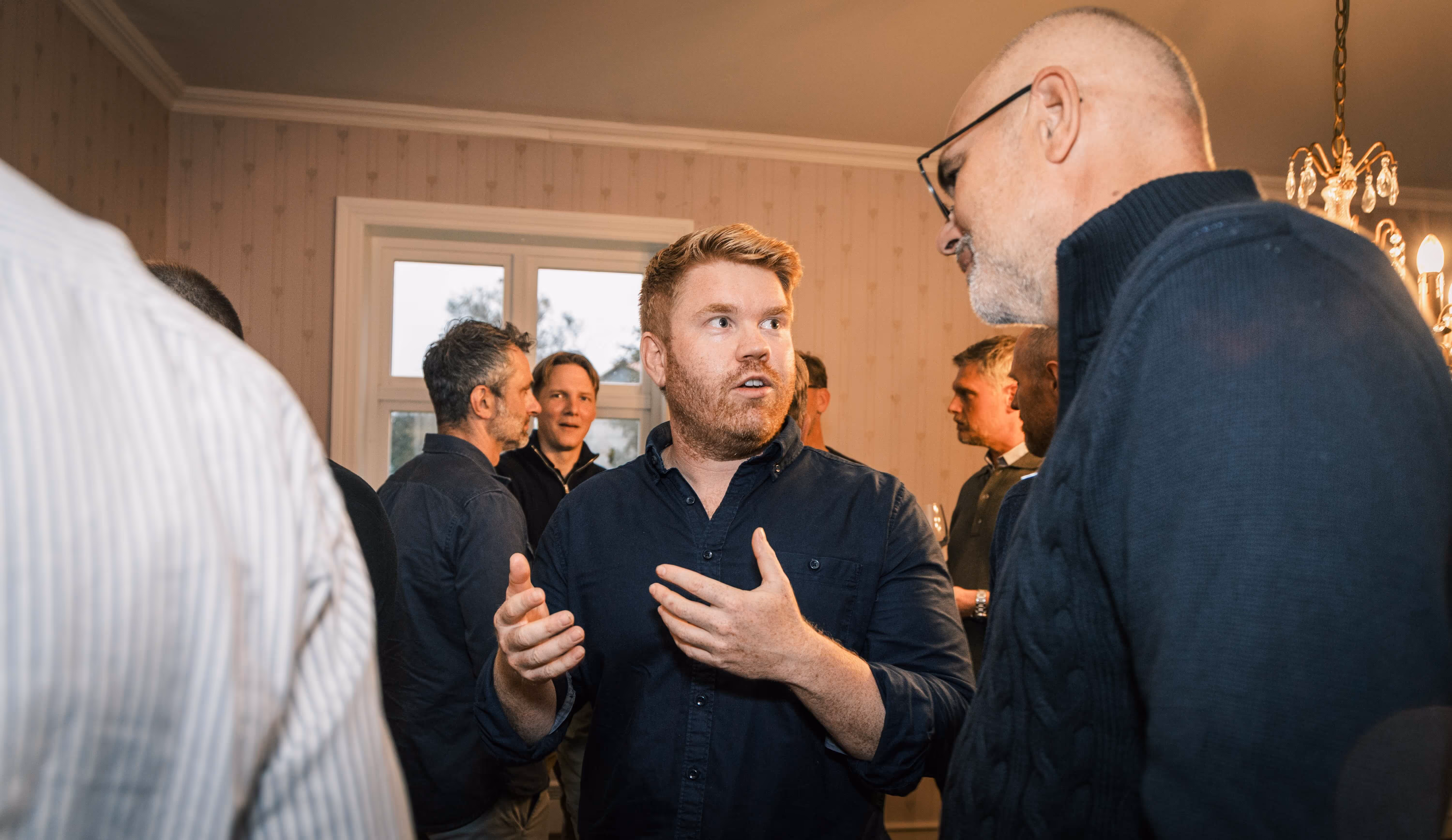 Group of men engaged in conversation indoors, with one man gesturing while speaking.