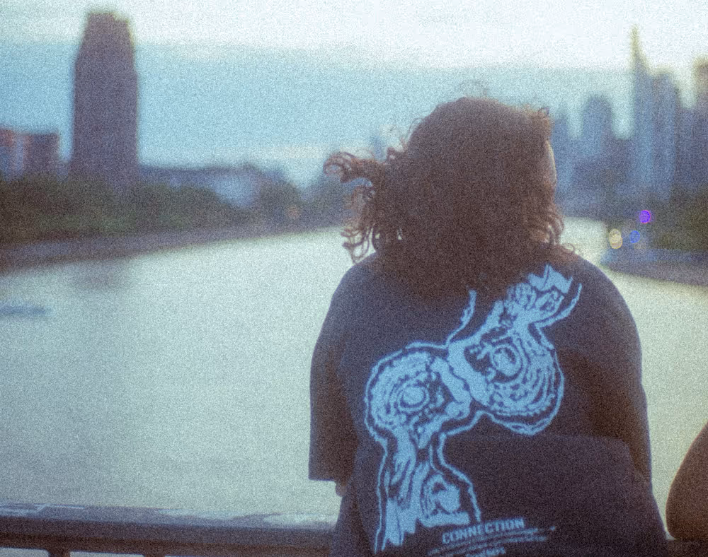Renée Customs T-Shirt am Flussufer mit Skyline im Hintergrund – Produktaufnahme