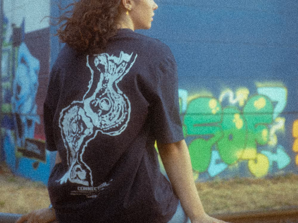 Renée Customs T-Shirt getragen, Person sitzt entspannt an urbaner Location – Produktfoto