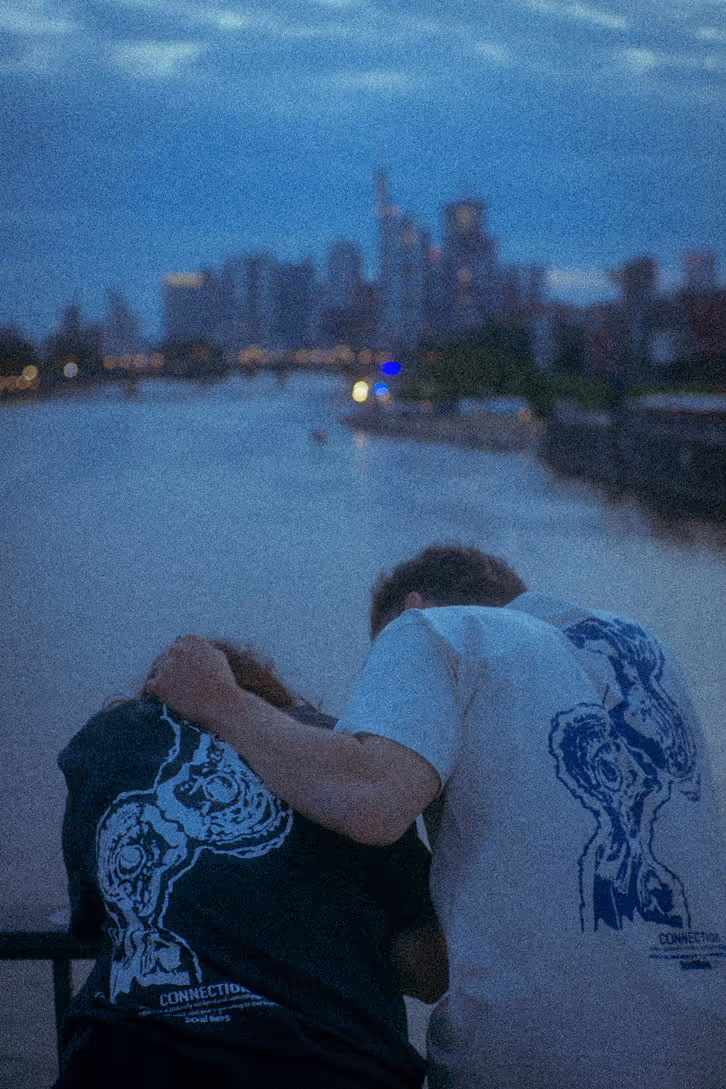 Renée Customs T-Shirt am Flussufer mit Skyline im Hintergrund – Produktaufnahme