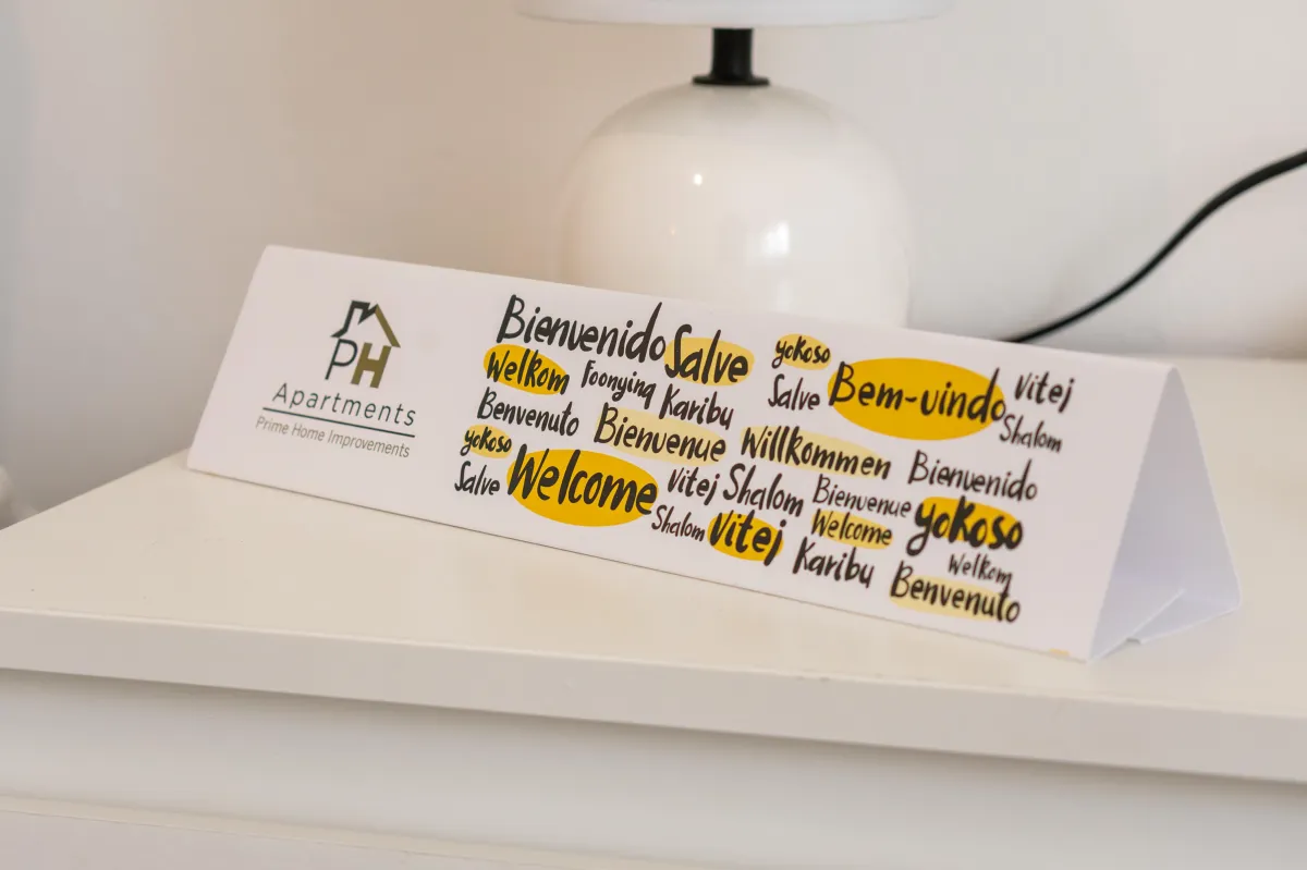 Table tent card on a white surface with 'PH Apartments Prime Home Improvements' logo and the word 'welcome' in various languages including English, Spanish, and German.