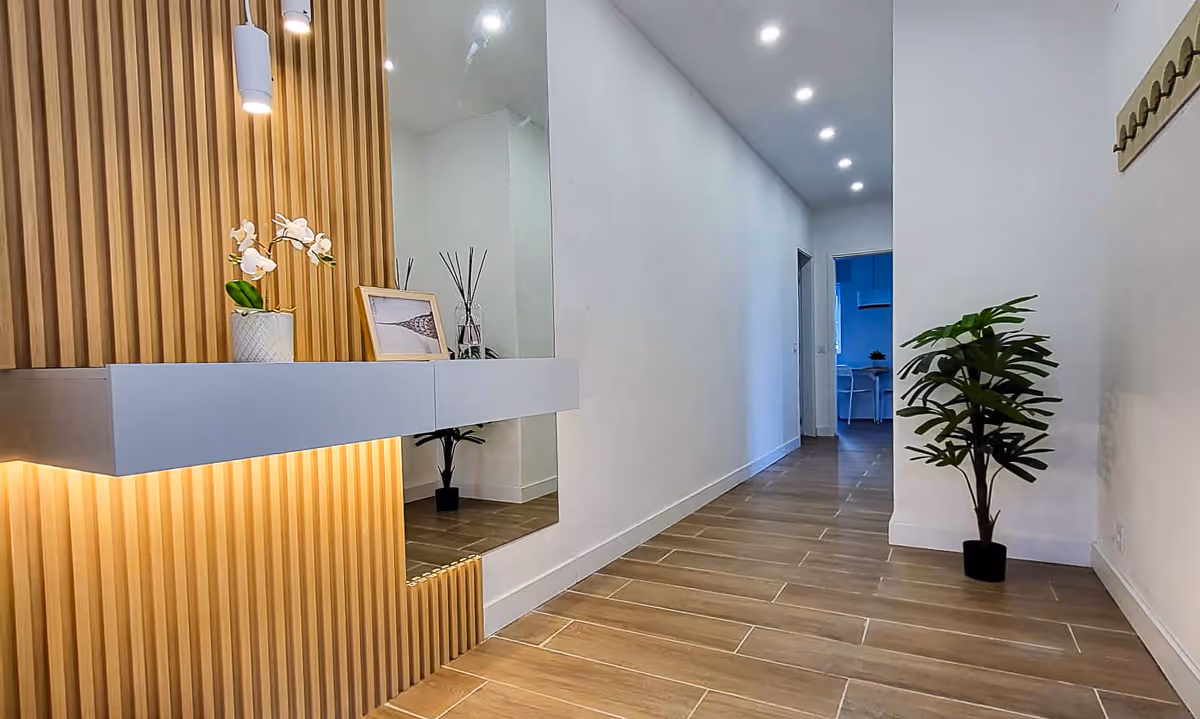 Corredor do apartamento Elegance I com painéis de madeira e iluminação ambiente