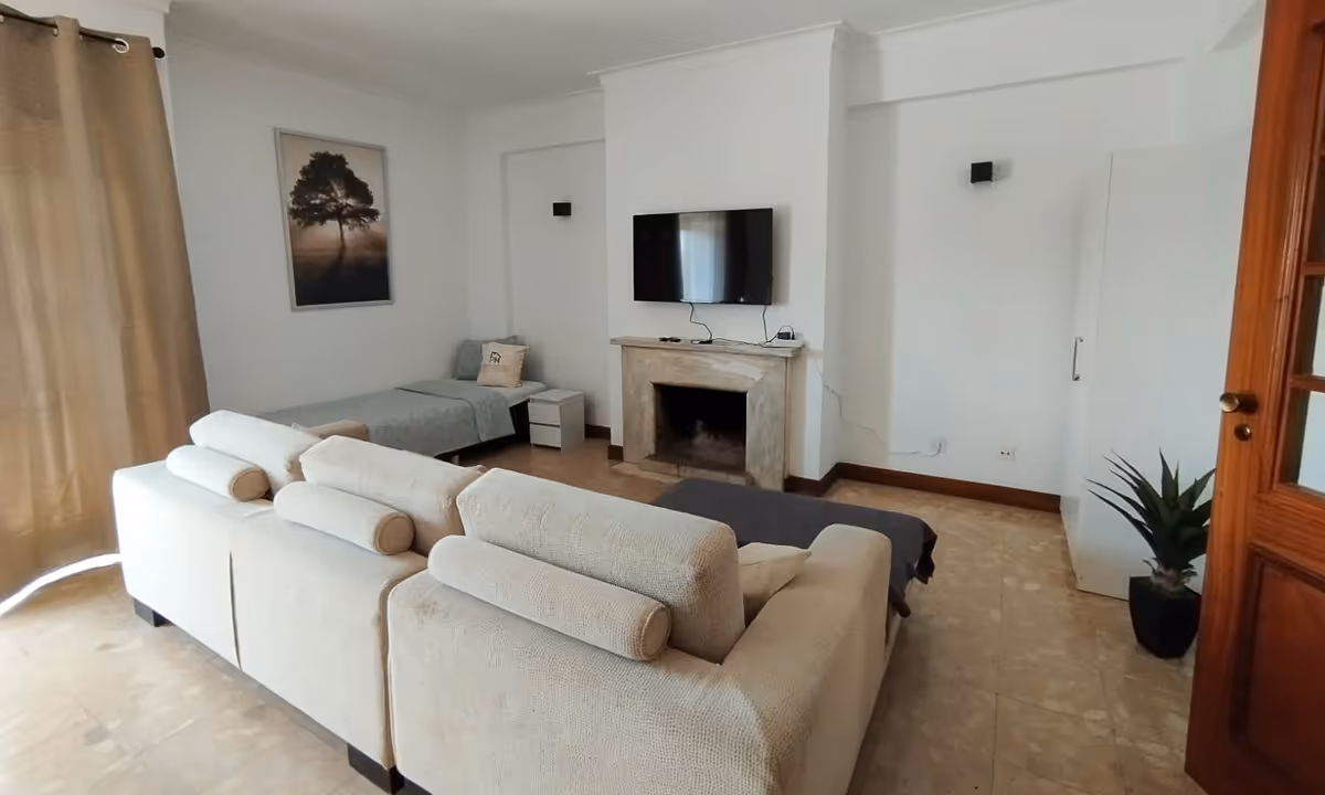 Sala de estar do apartamento Domus III com sofá bege, lareira e televisão