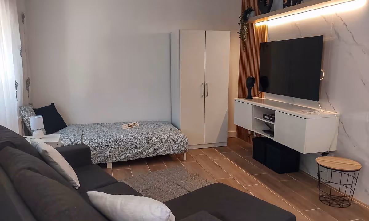 Sala de estar do apartamento Elegance II no Fundão com sofá, televisão e cama de solteiro