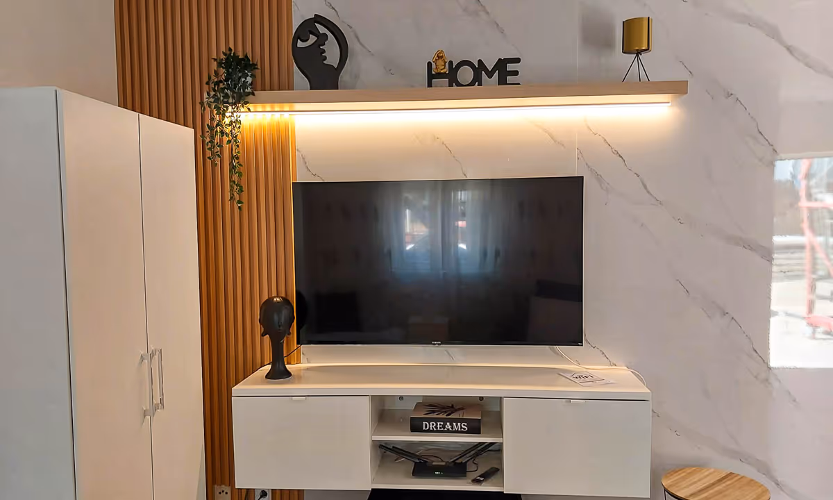 Detalhe da sala do apartamento Elegance II com televisão e prateleira decorada