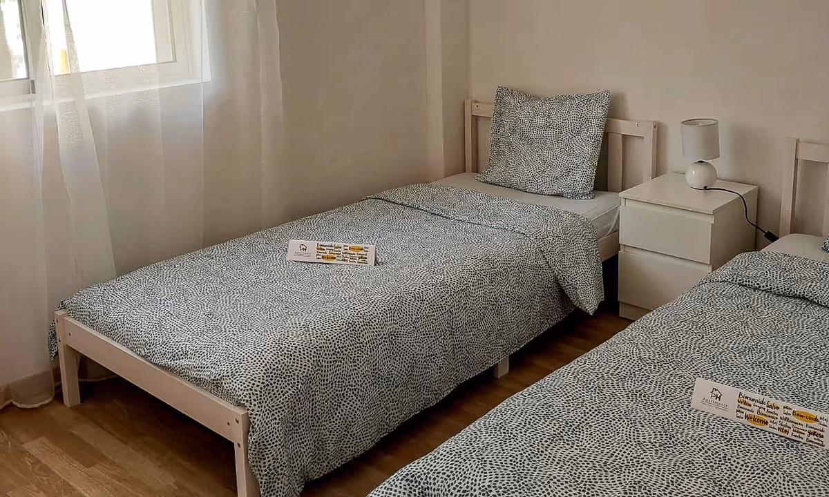 Quarto duplo do apartamento Elegance II com roupa de cama cinzenta e cortinas brancas