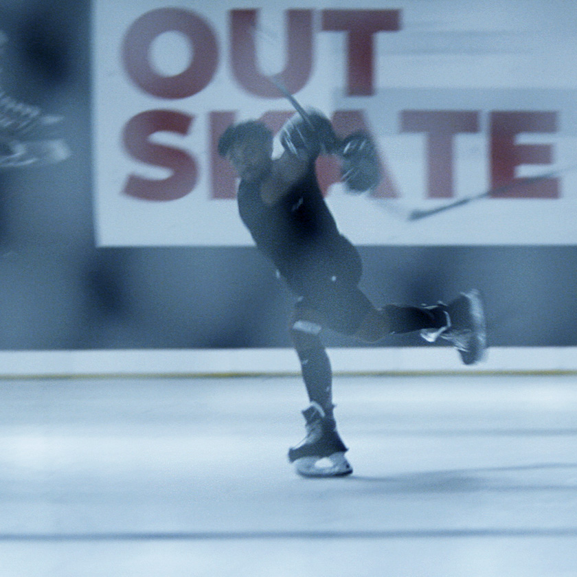 An Ice Hockey Player is shooting a puck with his stick while sliding on one food over Glice Synthetic Ice.