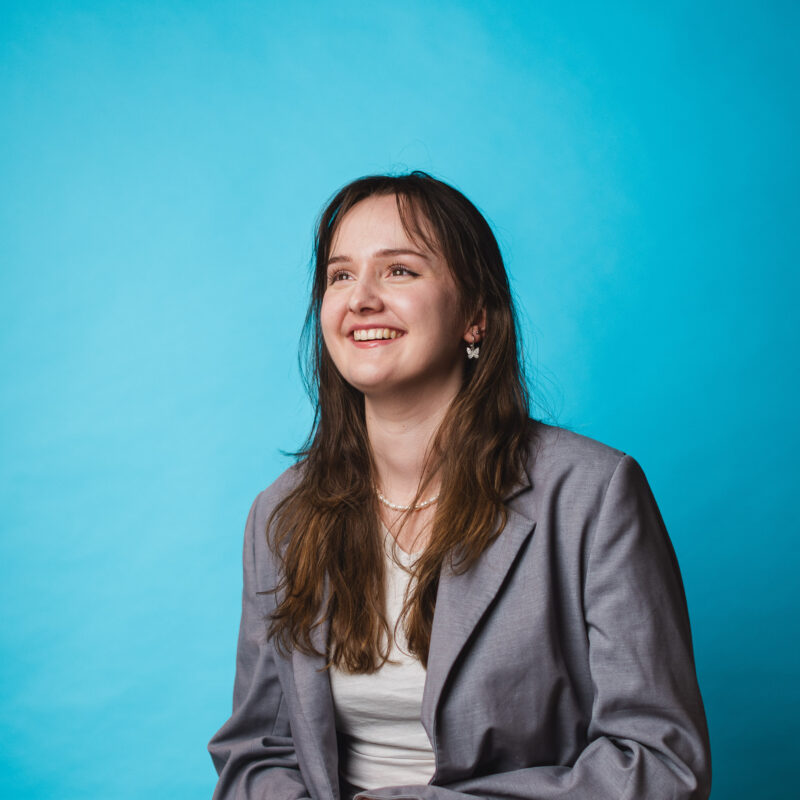 Maxine Buchert, CEO and Founding Partner, in a grey suit, in front of a turquoise background