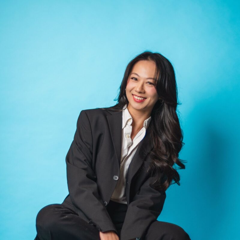 Trang Nguyen, Founding Partner, in a black suit, in front of a turquoise background