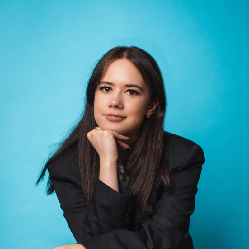 Valerie Kolganova, Founding Partner, in a black suit, in front of a turquoise background