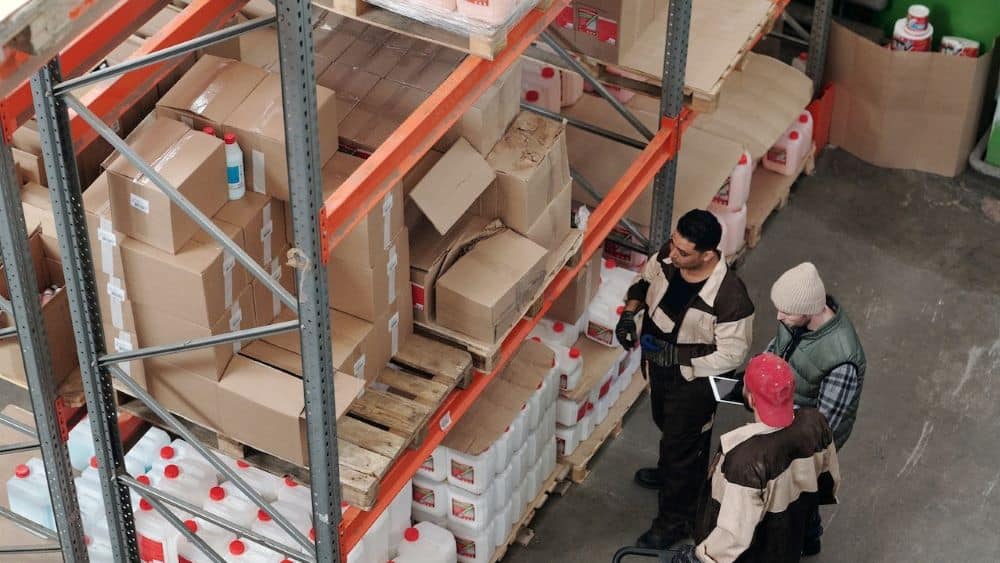 3 men standing near racks of boxes