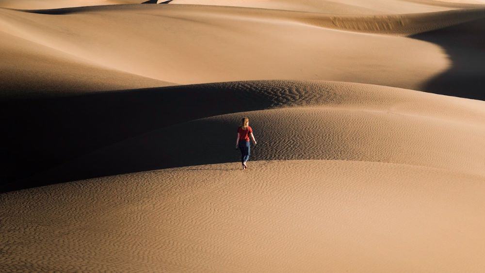 Lady in red top and blue jeans walking through a desert