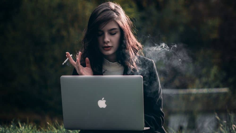 Lady smoking cigarettes while working on laptop