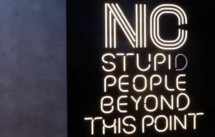 Neon sign on a dark wall that reads: "No stupid people beyond this point."