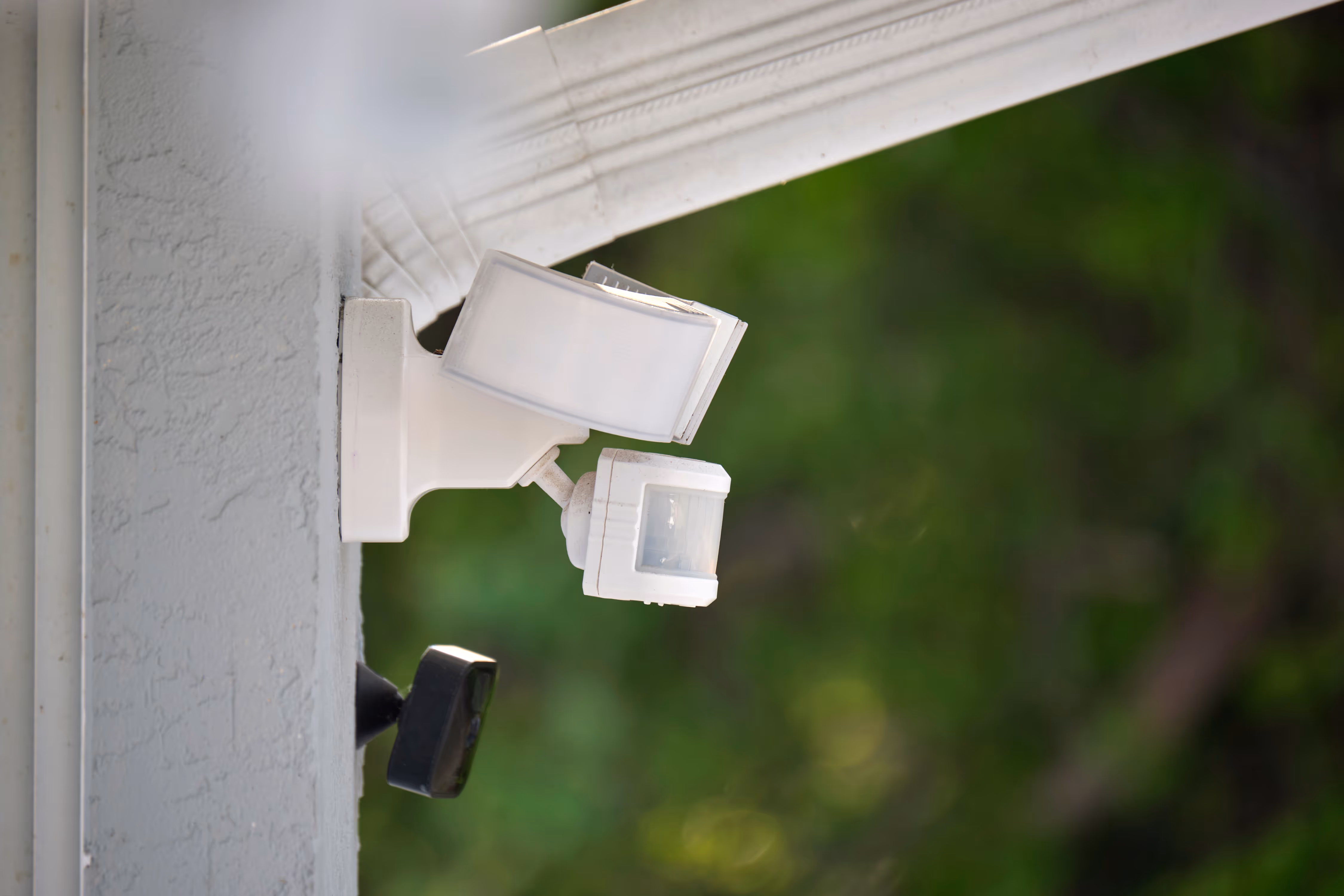 Gros plan sur un projecteur extérieur blanc équipé d’un détecteur de mouvement, installé sur la façade d’une maison, illustrant un système de sécurité et de protection à Bordeaux.