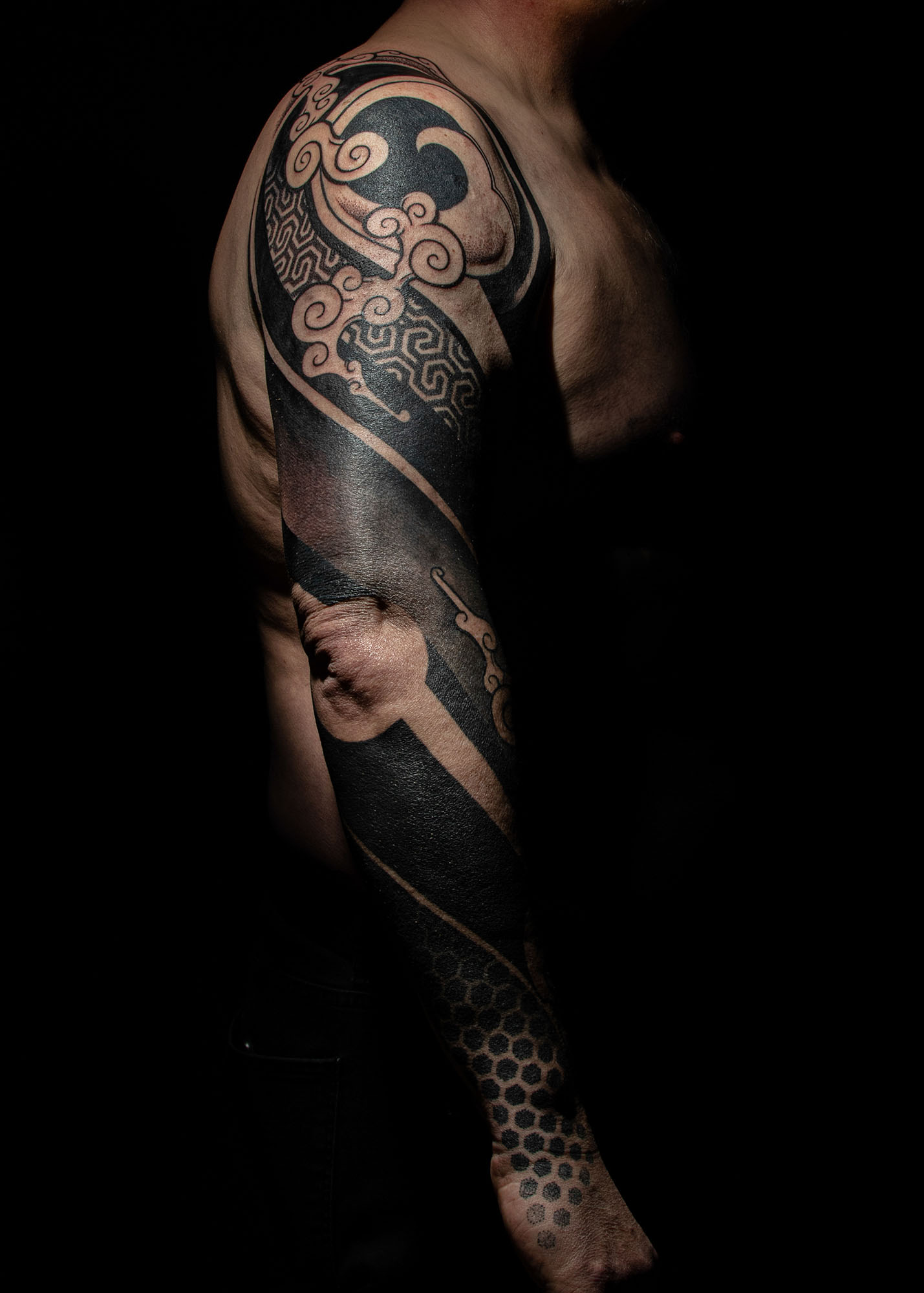 Arm mit einem ganzflächigen schwarzen Tattoo, das komplexe Muster und geschwungene Linien umfasst.
