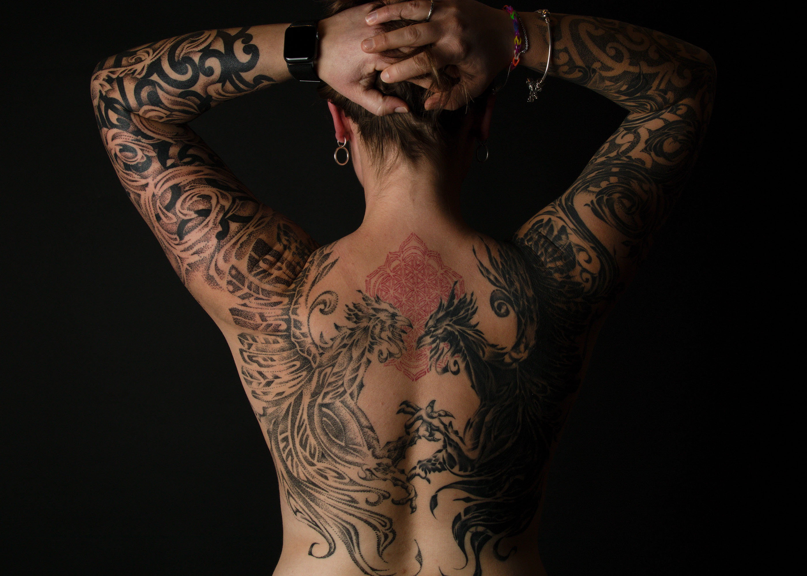 Person mit ausgedehnten, detaillierten schwarzen und roten Tattoos auf dem Rücken und den Armen, die phönixähnliche Vögel und geometrische Muster zeigen.