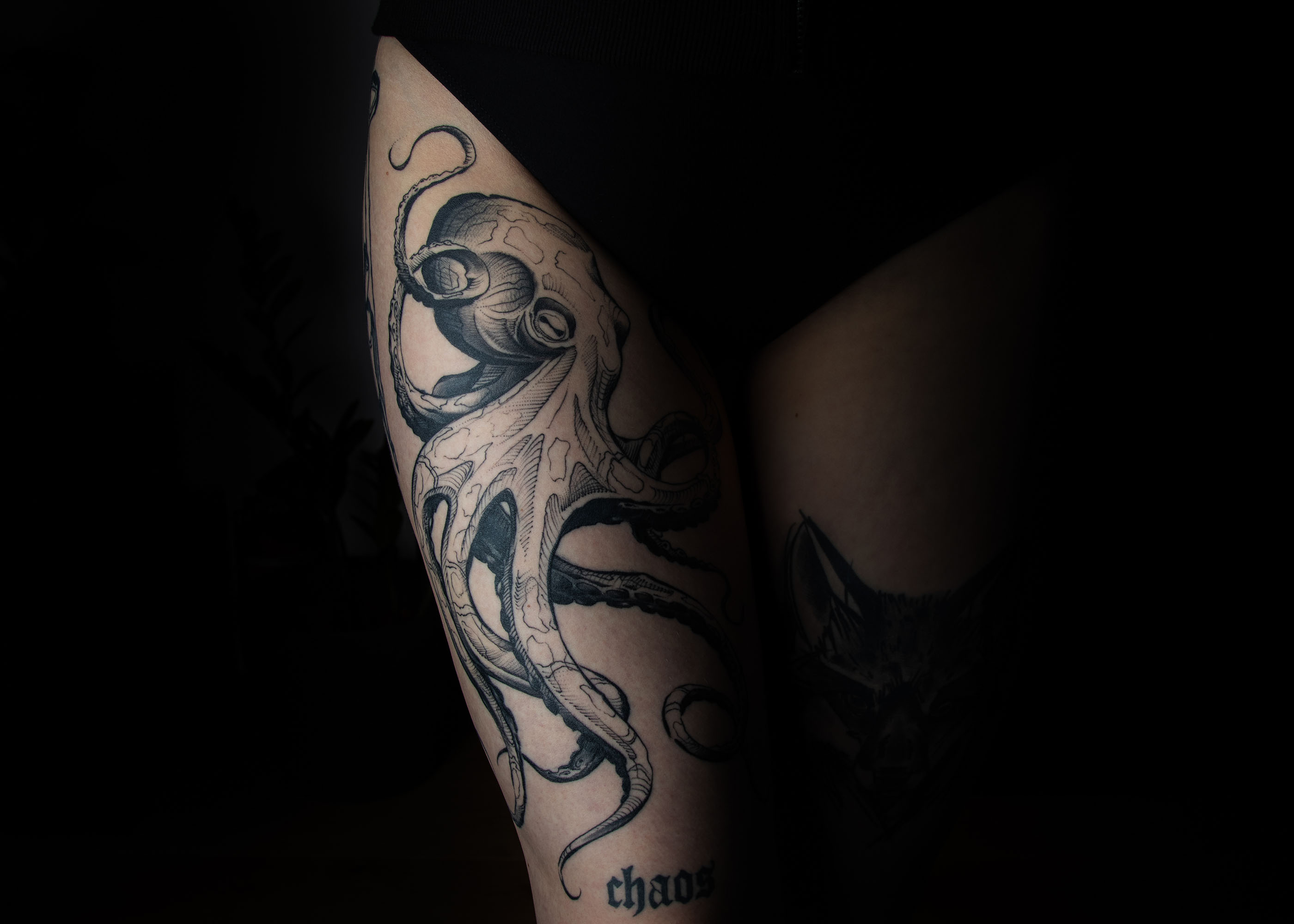 Tattoo eines detaillierten Oktopus auf einem Bein mit dem Wort 'chaos' darunter.