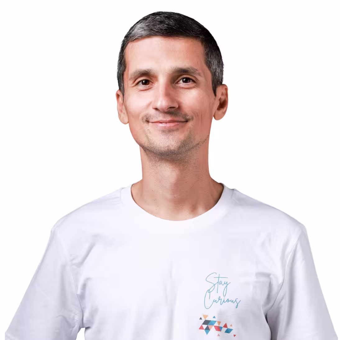 Un uomo sorridente con i capelli corti e scuri indossa una maglietta bianca. Sul petto, in primo piano, spicca la scritta «Stay Curious» circondata da forme geometriche colorate su sfondo bianco.