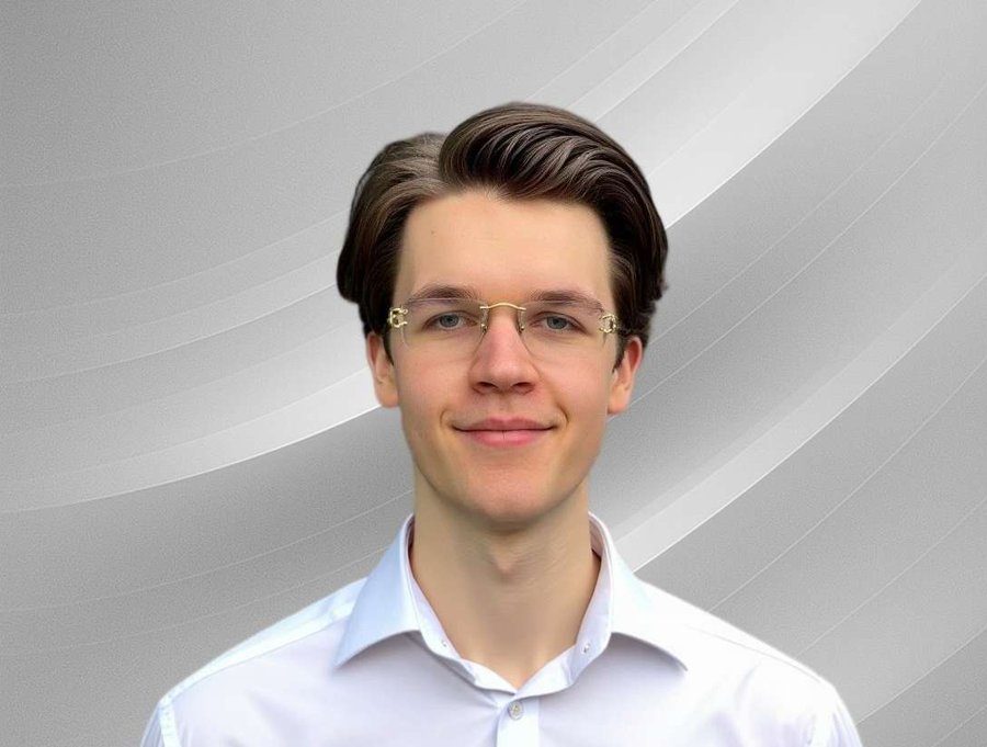 Porträt eines jungen Mannes mit weißem Hemd und Brille vor einem futuristisch hellgrauen, geschwungenen Hintergrund – freundlich, professionell und modern.