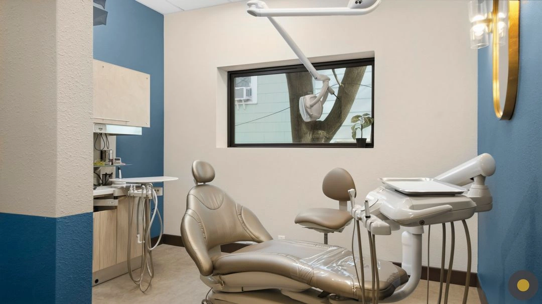 Modern dental office interior design featuring a comfortable treatment chair, natural light, blue accent walls, and integrated dental equipment in a functional operatory.