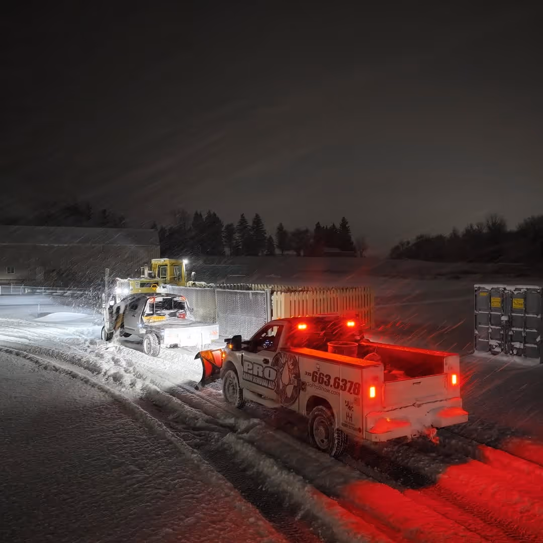 2 Pro Snow Removal snowplow trucks plowing a commercial property in Syracuse, NY at night while it snows