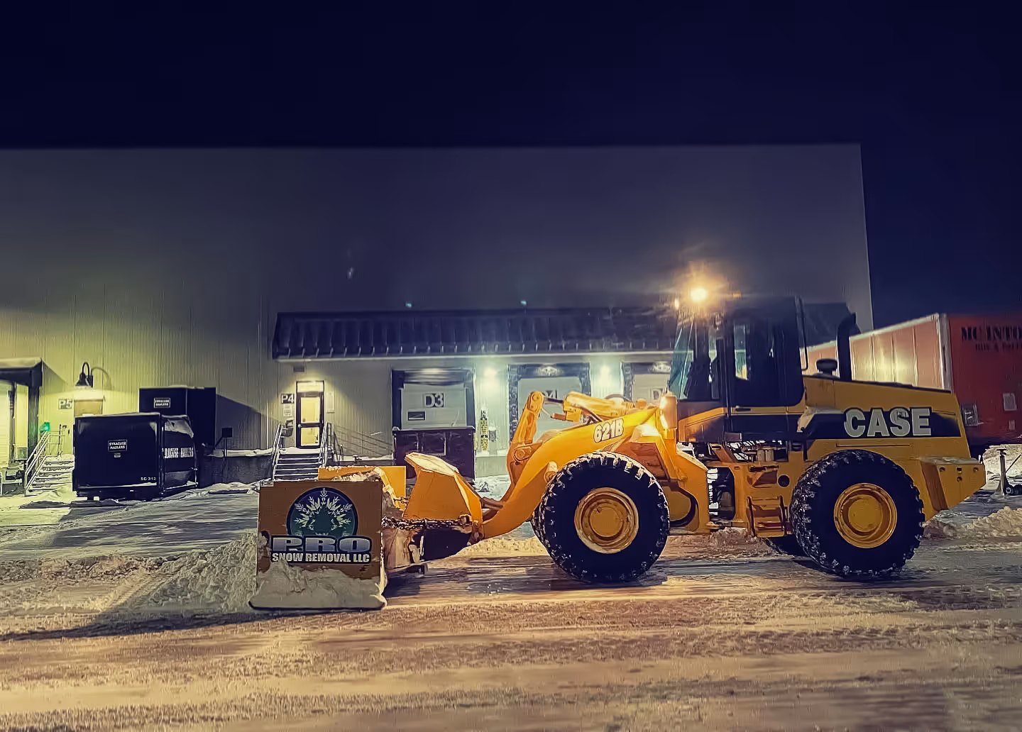 A Pro Snow Removal loader pushing snow in a Syracuse industrial facility at night