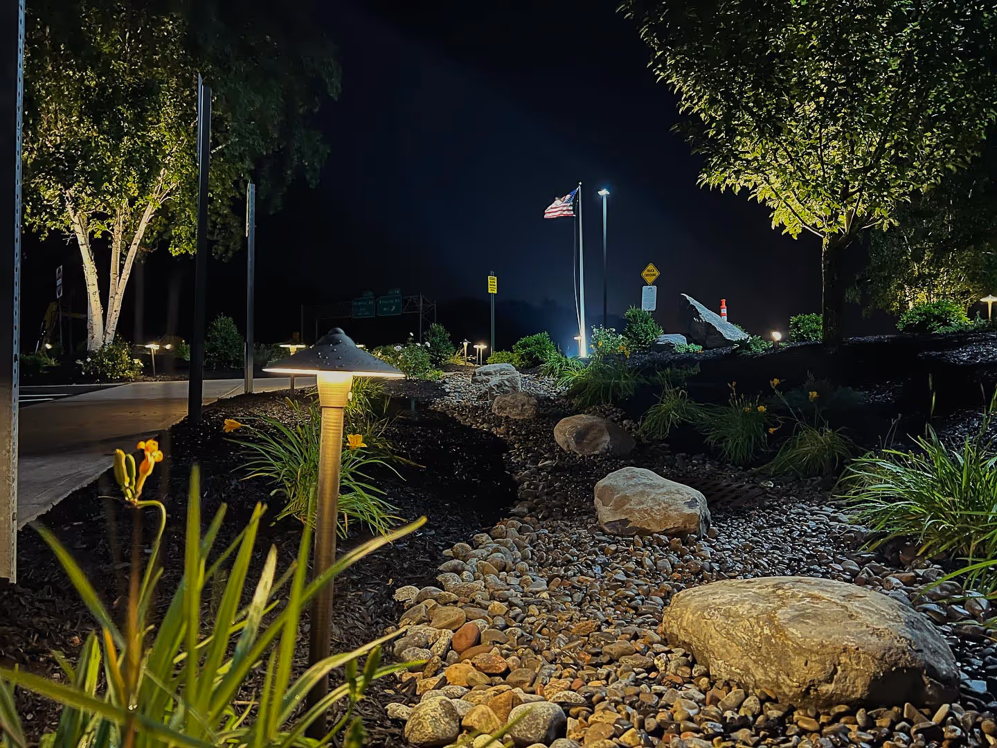 nighttime image of a commercial landscaping job performed in Syracuse, NY with warm lighting, plantings, and flower beds