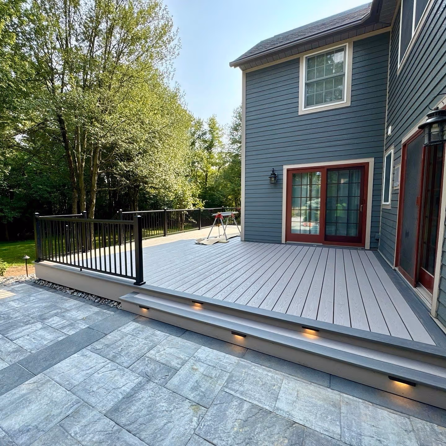 A new gray back deck installed beside a paver patio on a property in Whitesboro NY