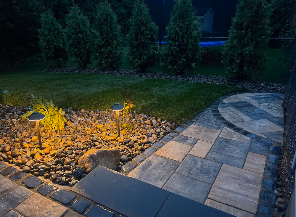 A Skaneatles walkway with lighting at night with custom stone hardscaping and calm warm lighting