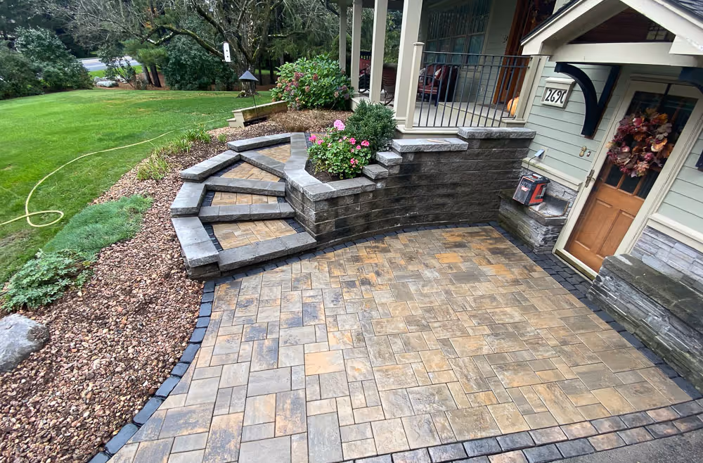 A curved hardscape staircase in front of a home with a stone patio and flower beds