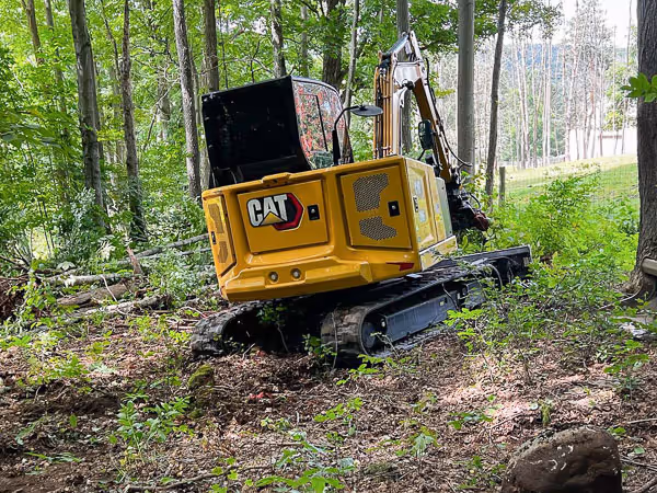 A CAT excavator clearing brush on a slight hill in Liverpool, NY
