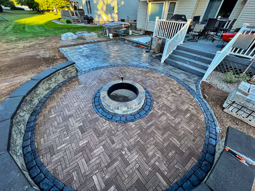 Custom hardscape patio beside a back porch with circular stone seating and a firepit in Manlius, NY