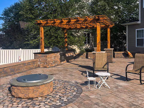 A wooden pergola, firepit, outdoor kitchen, and stone patio installed by PSR in Syracuse, NY