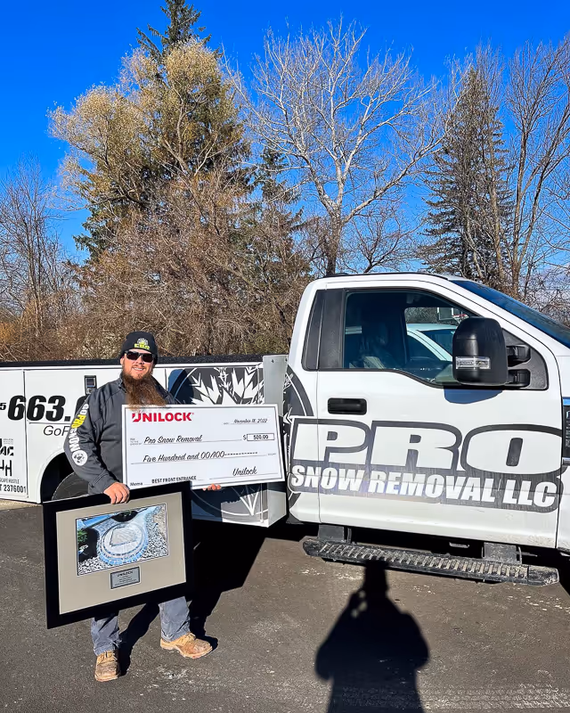A photo of Pro Snow Removal owner Michael Johnson holding an award and check awarded to PSR from Unilock