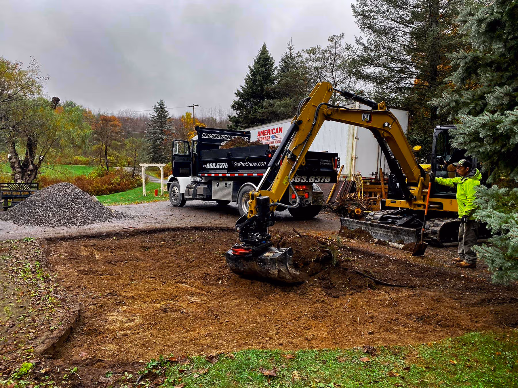 A PSR excavator and truck digging out a hole in a yard beside a driveway