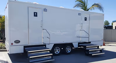 White portable restroom trailer with two separate entrances and staircases, parked outdoors under a clear sky.