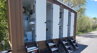 Outdoor mobile restroom trailer with multiple stalls, each with a small staircase leading up to the entrances.