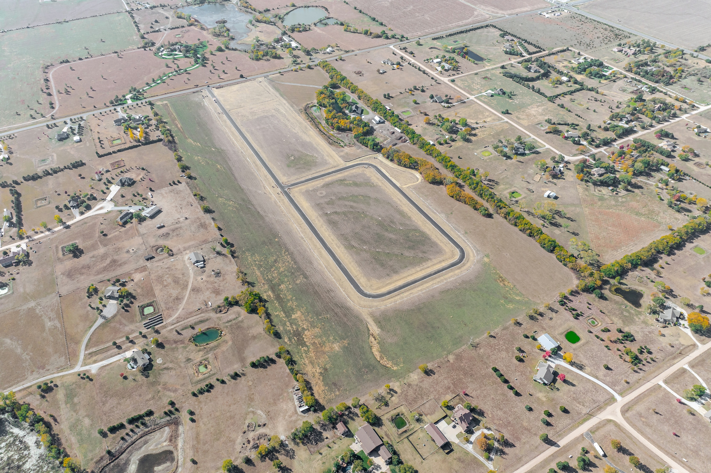 Aerial view of rural farmland with scattered houses, ponds, tree lines, and open fields.