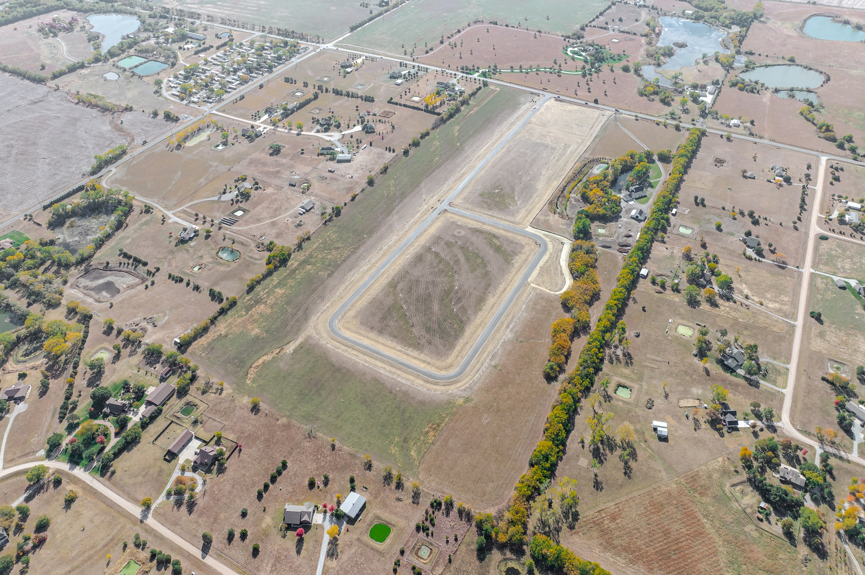 Aerial view of a rural area with scattered houses, dirt roads, small ponds, and a large rectangular dirt track in the center.