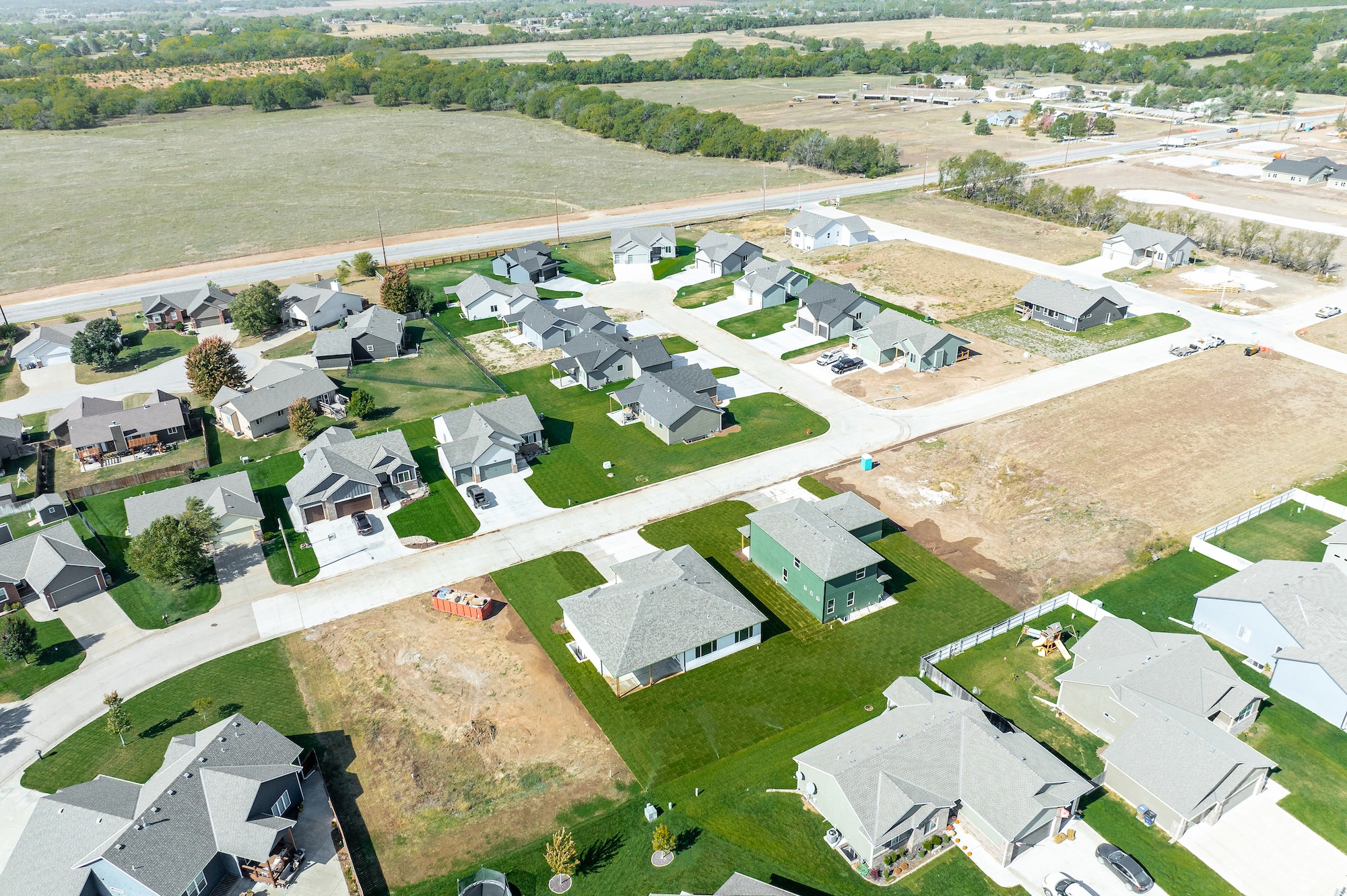 Aerial view of a suburban neighborhood with single-family houses, green lawns, and open fields.