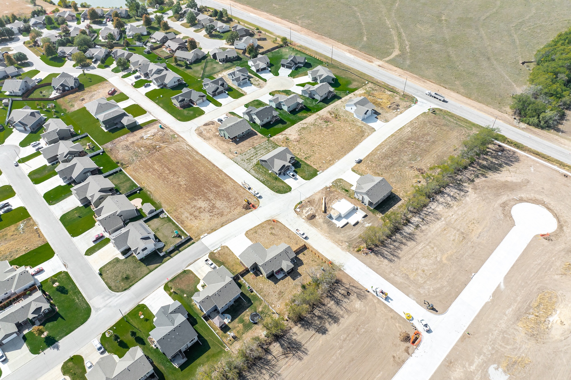 Aerial view of a residential neighborhood with newly built houses, green lawns, and some vacant lots with construction equipment.