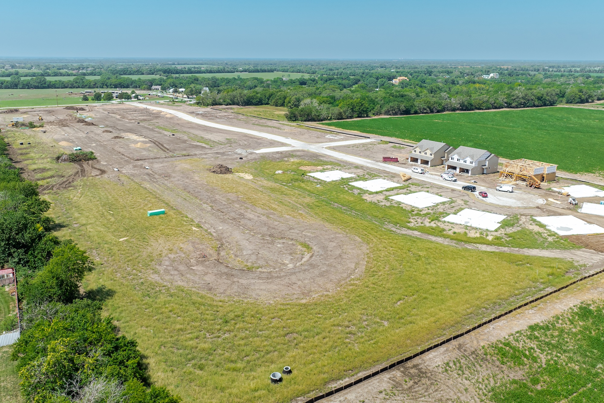 Aerial view of a residential construction site with newly built houses, building foundations, and surrounding farmland.