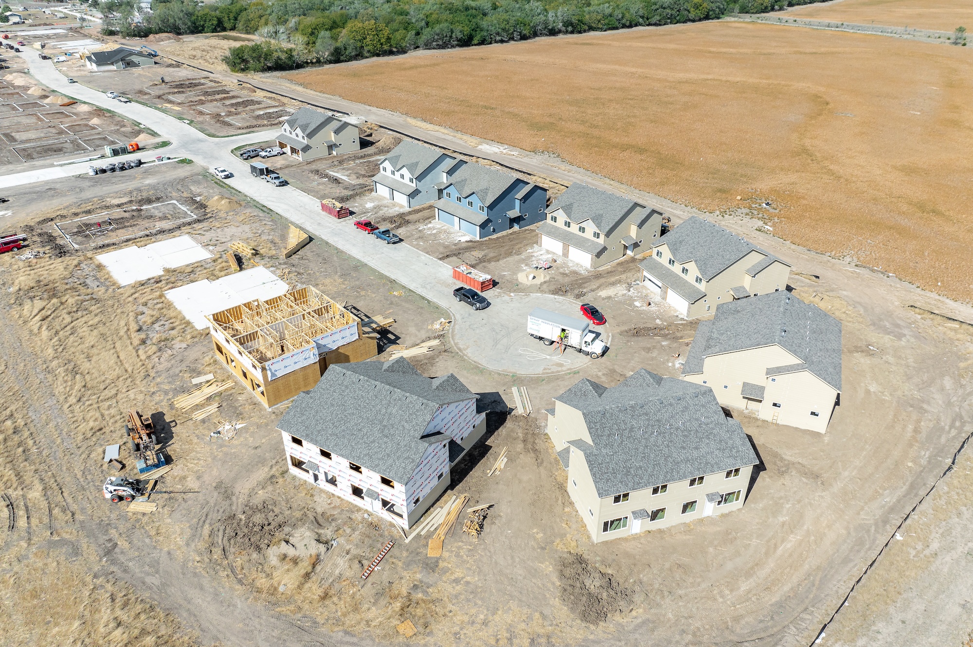 Aerial view of a suburban housing development with several completed and under-construction homes surrounded by dry grass fields.