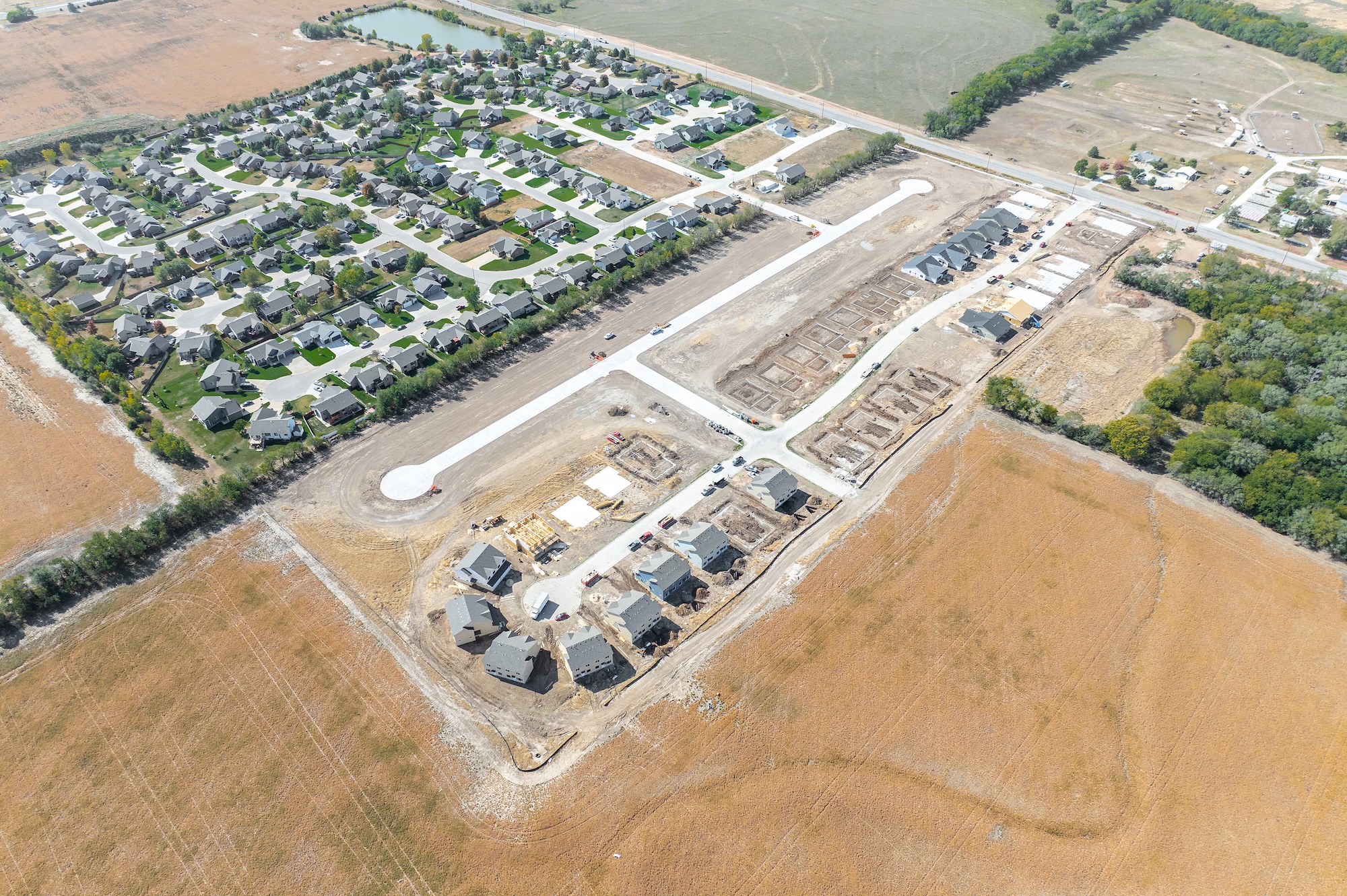 Aerial view of a residential neighborhood next to a housing development under construction surrounded by open fields and trees.